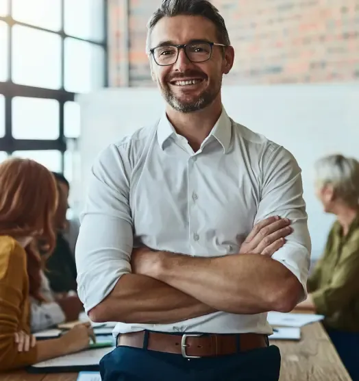 Adviser in glasses standing with folded arms in front of colleagues at a meeting