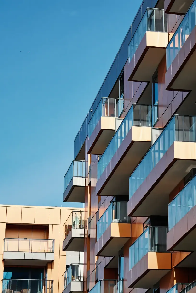 Fasade på en moderne boligblokk med glassbalkonger mot blå himmel